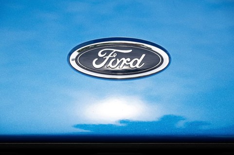 Logo of the car manufacturer Ford, sun behind clouds reflected in the paintwork