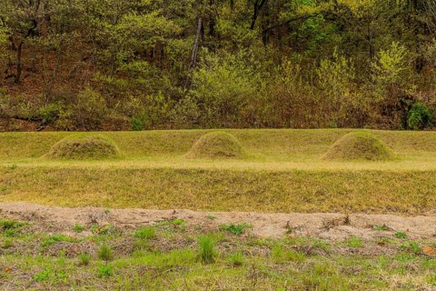 Three unmarked burial mounds at foot of tree covered mountainside, South Korea, South Korea, Asia