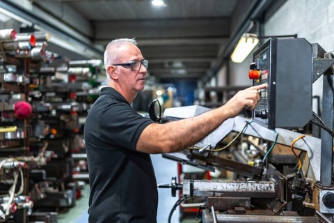 Man operating in the control station of a mechanical saw in a metal cnc factory