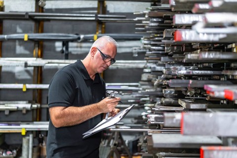 Mature caucasian man inspecting quality control of metal bars doing inventory at factory