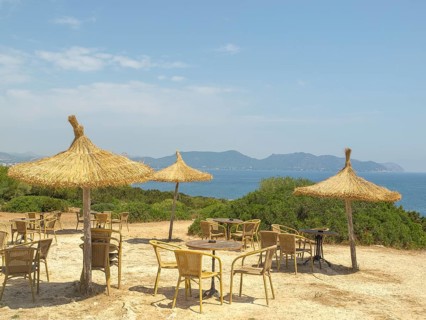Beach huts with straw parasols, tables and chairs, sea view and mountains in the background in