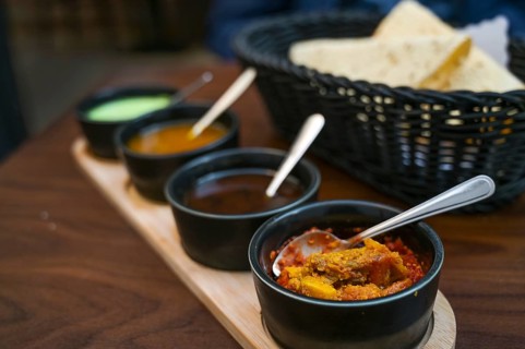 Indian dip, relish, chutney and sauce served in small black bowls with crispy papadam bread on a