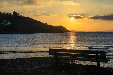 Bench on Le Caro beach shortly in front of sunset, view of the Presqu'ile de Crozon,