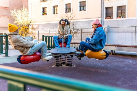 Three friends enjoying a sunny winter day, playing together on a playground seesaw in a city park