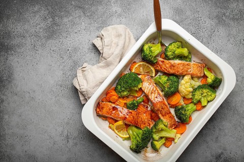 Top view of healthy baked fish salmon steaks, broccoli, cauliflower, carrot in casserole dish on