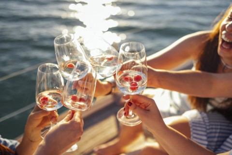 Female hands holding glasses of champagne with raspberries on board the boat. Sunset sky and sea on