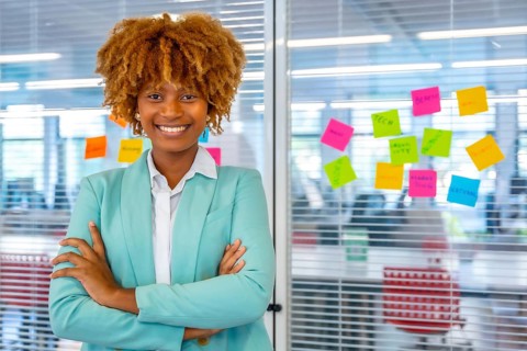 Portrait of a creative and young african woman standing with arms crossed next to a glass with