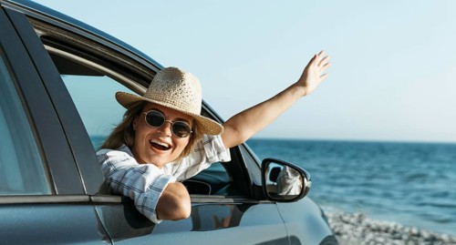 Happy blonde woman with hat looking out car window