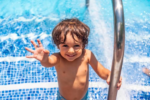 Two year old boy enjoying summer in a swimming pool, smiling on vacation from the water