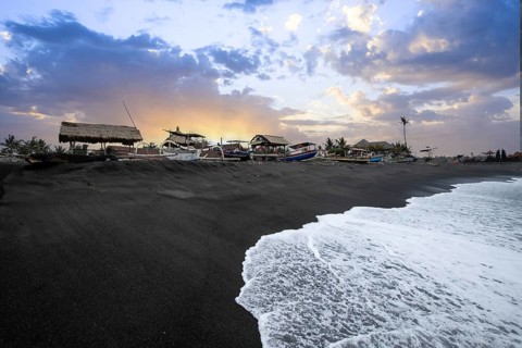 Traditional fishing boat Jukung, on a black sand beach directly by the sea. Sunset landscape by the
