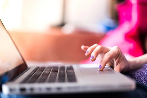 Girl with purple fingernails is using her laptop at home on the couch