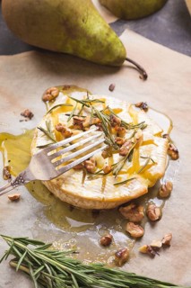 Piece of baked camambert on a fork. Delicious baked cheese with honey, walnuts, herbs and pears