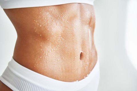 Close up belly of a beautiful sporty girl in drop of sweat or water on skin. Body care, fitness