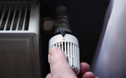 hand turning off thermostat on radiator to save energy due to increasing heating costs