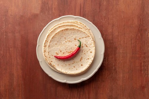 A red chili pepper, shot from above on a pile of tortillas, Mexican flatbreads, on a dark rustic