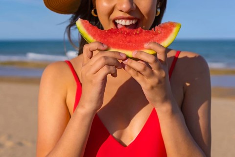 Portrait of a woman eating a watermelon by the beach. Cutout of mouth smiling with red bikini