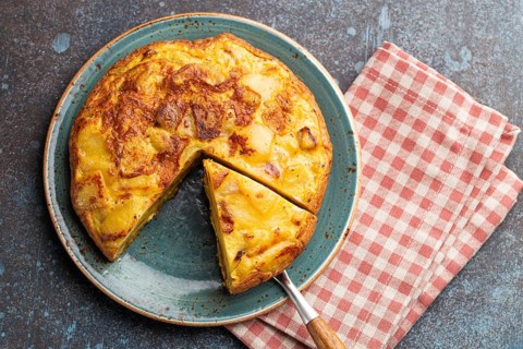 Homemade Spanish tortilla with one slice cut - omelette with potatoes on plate on stone rustic