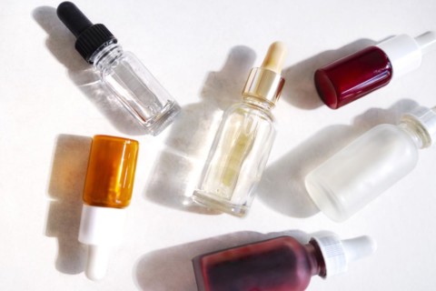 Serum with collagen and peptides in colorful glass bottles on light background with sunlight shadow