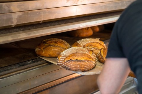 Male employee baker of bakery in workshop workshop of artisan bakery removing baked bread from oven