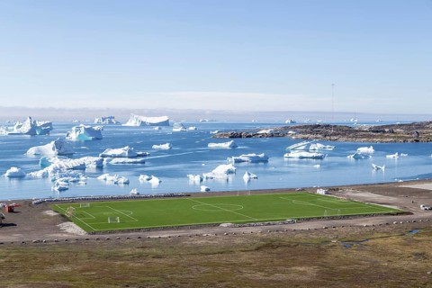 Qeqertarsuaq, Greenland, July 6, 2018: The local soccer field with icebergs in the background,