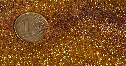 Coin of 1 Euro Rolling on Gold Powder against Black Background