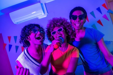 Happy multi-ethnic friends singing karaoke at night partying together at the apartment