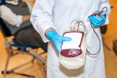 Part of and close-up of a healthcare worker showing a blood bag filled with a donation