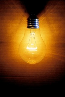 Closeup of an old burning light bulb, switched on, a carton as background is illuminated, lit with