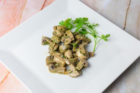 Herb-marinated mushrooms with parsley on a square white plate, typical food, typical mediterranean