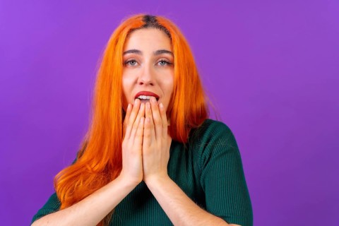 Redhead woman in studio photography making the gesture please on a purple background