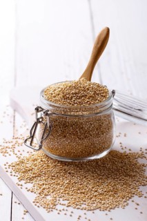 White quinoa seeds in a jar on white wooden table, closeup
