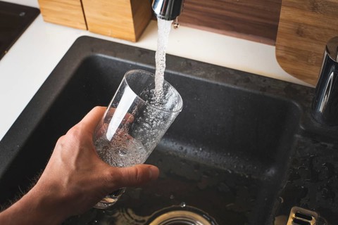 Filling glass of water from stainless steel kitchen faucet. Drinking water concept. Austria pure