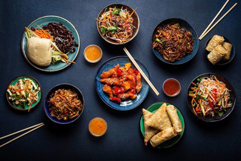 Set of assorted Chinese dishes on table: sweet and sour chicken on plate, fried spring rolls,