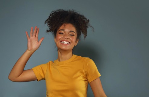 Beautiful happy dark skinned african american ethnicity woman in yellow tshirt raising hand in