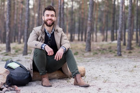 Portrait smiling male traveler sitting beach with his backpack