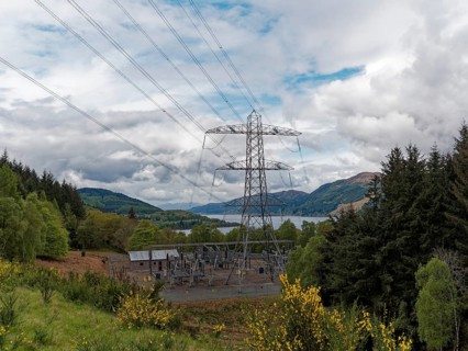 A power station in the middle of a natural landscape with electricity pylon and cloudy sky,