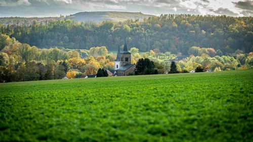 A picturesque view of a village with a church surrounded by autumn coloured trees and hilly