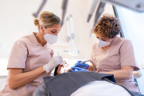 Dentist and assistant performing a mouth and tooth filling on a young client in the modern dental