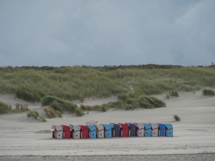 Row of colourful beach chairs along a sandy beach with high dunes in the background under a cloudy