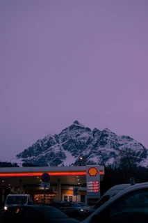 Shell petrol station in the foreground at dusk, snow-covered Serles mountain peaks in the
