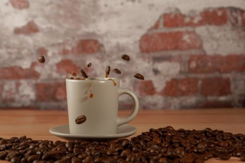Appetizing cup of coffee with coffee beans splashing on a wooden table with a brick background