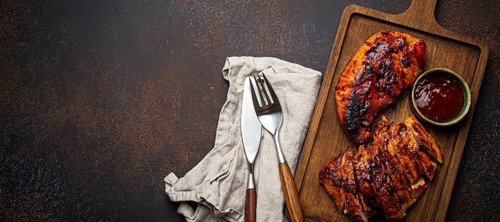 Grilled turkey or chicken marinated fillet with red sauce served and sliced on wooden cutting board