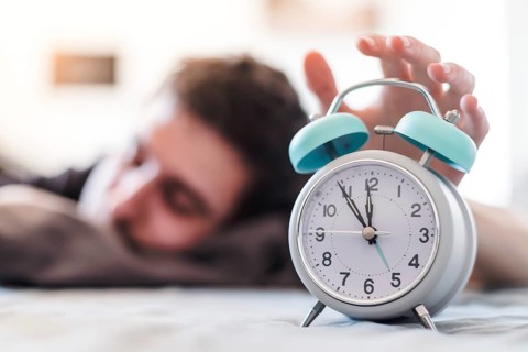 White alarm clock in the morning. Young man wakes up