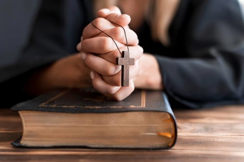 Person praying with cross holy book