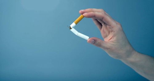 Hand breaking a cigarette against blue background