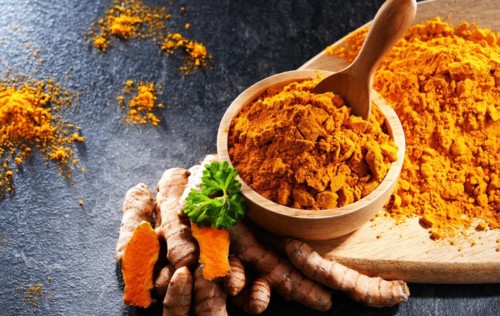 Composition with a bowl of ground turmeric and its fresh rhizome