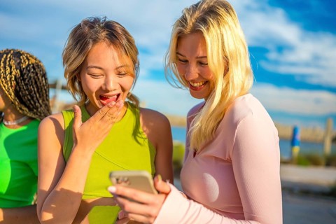 Chinese woman and blonde female friend sharing a mobile