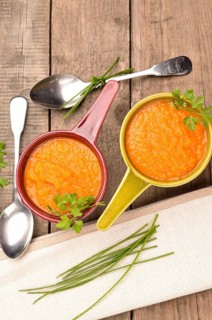 Top view of two rustic bowls with carrot soup on a wooden table