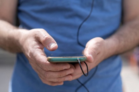 Close-up of a man's hands holding his phone with the headphones connected