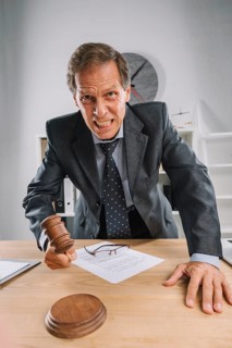 Angry mature judge striking his gavel table courtroom